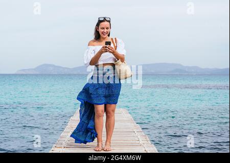 Lächelnde Frau, die Smartphone benutzt, während sie auf dem Steg steht Stockfoto