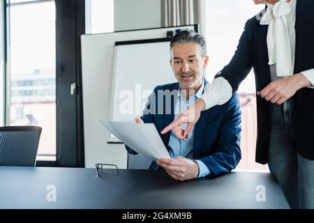 Geschäftsfrau, die auf das Dokument verweist, während sie mit einem männlichen Kollegen im Vorstandszimmer spricht Stockfoto