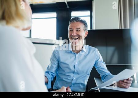 Fröhlicher männlicher Profi, der eine Kollegin anschaut, während er im Büro diskutiert Stockfoto