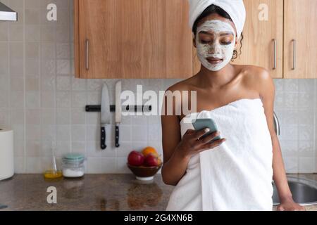Junge Frau, die in der Küche ein Handtuch mit dem Mobiltelefon trägt Stockfoto