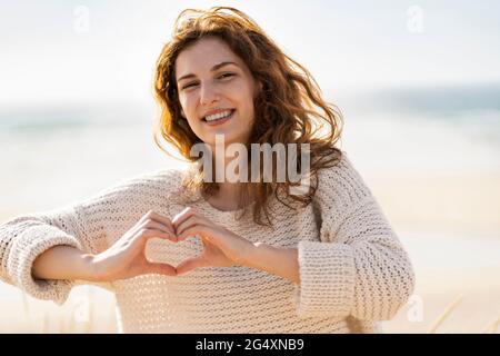 Lächelnde schöne Frau, die an sonnigen Tagen Herzform formt Stockfoto