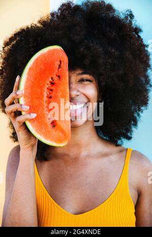 Verspielte junge Frau mit Wassermelonenscheibe vor dem Gesicht Stockfoto