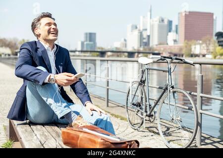 Glücklicher, reifer Geschäftsmann, der während der Sonne am Fluss sitzt Stockfoto