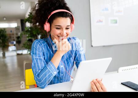 Unternehmerin mit Kopfhörern, die im Kreativbüro am digitalen Tablet arbeitet Stockfoto