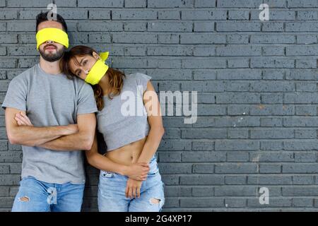 Freundin lehnte sich vor einer grauen Wand auf ihren Freund mit verbundenen Augen Stockfoto