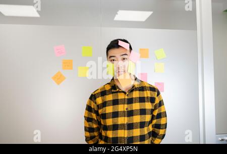 Junger Geschäftsmann steht mit Haftnotizen auf dem Gesicht Stockfoto