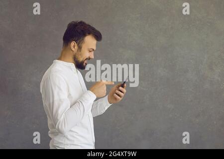 Seitenansicht eines glücklichen Mannes mit Mobiltelefon, das isoliert auf grauem Hintergrund im Kopierbereich steht Stockfoto