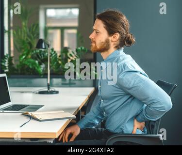 Männlicher Büroangestellter, der unter schrecklichen Schmerzen im unteren Rücken leidet Stockfoto