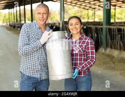 Bauernpaar, das Milchkännen im Kuhstall auf dem Milchviehbetrieb hält Stockfoto