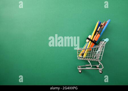 Kauf von Schulgeräten mit einem Wagen voller Vorräte auf grünem Hintergrund. Draufsicht. Stockfoto