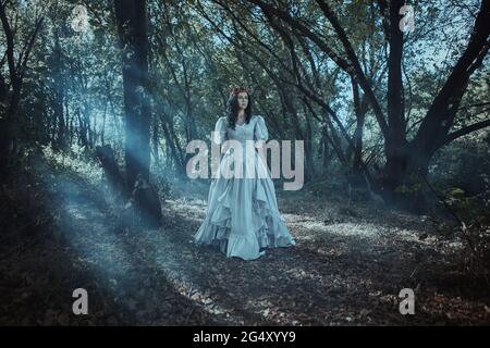 Schöne Dame in einem weißen historischen Kleid und roter Krone im Wald Stockfoto
