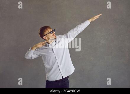 Junger Geschäftsmann in einer zermetzten Lebensbrille, die vor grauem Studiohintergrund tänzelte Stockfoto