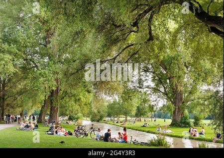 München - Bayen- Deutschland, 11. Juni 2021: Menschen, die sich im Gras entspannen und Sport treiben wie Radfahren auf dem Eisbach. Am Wochenende gingen viele zu den en Stockfoto