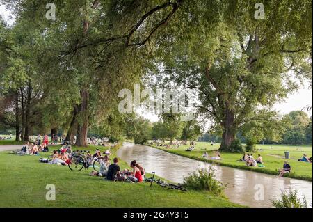 München - Bayen- Deutschland, 11. Juni 2021: Menschen, die sich im Gras entspannen und Sport treiben wie Radfahren auf dem Eisbach. Am Wochenende gingen viele zu den en Stockfoto