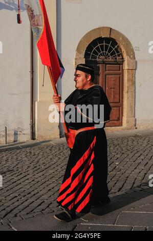 Dieses prächtige, schwarz-rote mittelalterliche Klerikkostüm erinnert an die illustre Geschichte von Anagni, Latium, Italien, als Stadt der Päpste, dem Sommersitz zwischen dem 11. Und 14. Jahrhundert der Päpste, die seine relative kühle gegenüber der schwellenden Hitze Roms bevorzugten. Anagni war auch der Geburtsort der Päpste Gregory IX und Boniface VIII. Der Standard für die Cellere Contrada (traditionelles Viertel) der Stadt wird in einer Prozession zu Ehren des Bischofs und Märtyrers San Magno di Anagni (Heiliger Magnus von Anagni) aus dem 3. Jahrhundert n. Chr., des schutzpatrons der Stadt, dargestellt. Stockfoto