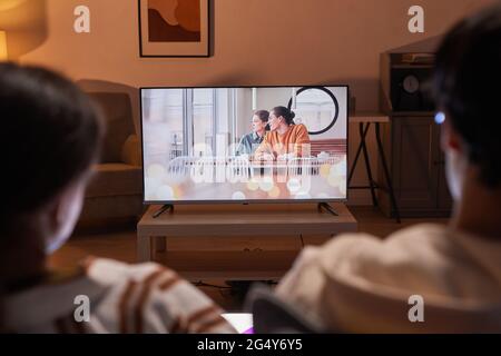 Rückansicht eines erwachsenen Paares, das zu Hause Filme ansieht, während es auf dem Sofa sitzt, Fokus auf den Fernsehbildschirm Stockfoto