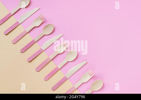 Einweg-Bambuslöffel, Gabeln und Messer auf gelbem und rosa Hintergrund. Zero Waste Konzept. Draufsicht, Kopierbereich. Stockfoto