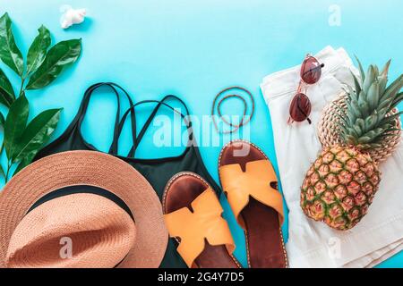 Damen Sommerkleidung, Accessoires, Hausschuhe und Ananas auf blauem Hintergrund. Beauty, Mode, Sommerurlaubskonzept. Draufsicht, flach liegend, Copy Spa Stockfoto