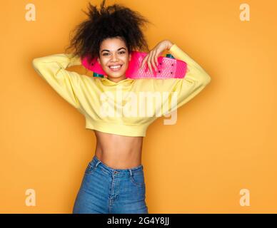 Cooles Mädchen mit Skateboard auf gelbem Hintergrund Stockfoto