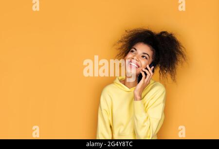 Mädchen spricht am Telefon und lächelt. Foto von afroamerikanischen Mädchen auf gelbem Hintergrund Stockfoto