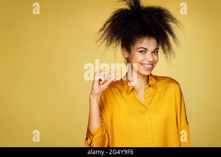 Ein wenig. Schönes Mädchen zeigt etwas kleines, winziges unsichtbares Objekt. Foto von afroamerikanischen Mädchen auf gelbem Hintergrund Stockfoto