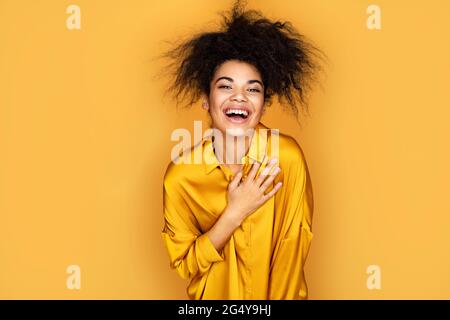 Überfröhliches Mädchen hält ihre Hand am Herzen, kann nicht aufhören zu lachen. Foto von afroamerikanischen Mädchen auf gelbem Hintergrund Stockfoto