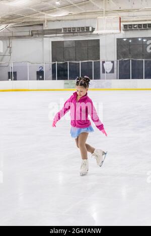 Kleines Mädchen, das Eiskunstlauf auf einer Indoor-Eisbahn übt. Stockfoto