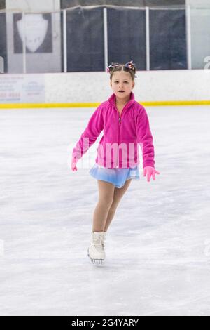 Kleines Mädchen, das Eiskunstlauf auf einer Indoor-Eisbahn übt. Stockfoto