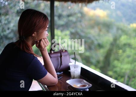 Die wunderschöne Thailänderin sitzt in einer Cafeteria auf einem Hügel und genießt die Landschaft Stockfoto