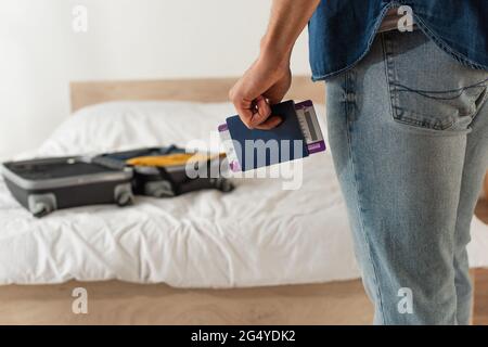 Beschnittene Ansicht des Mannes, der Pass und Flugticket in der Nähe von verschwommenem Koffer auf dem Bett hält Stockfoto