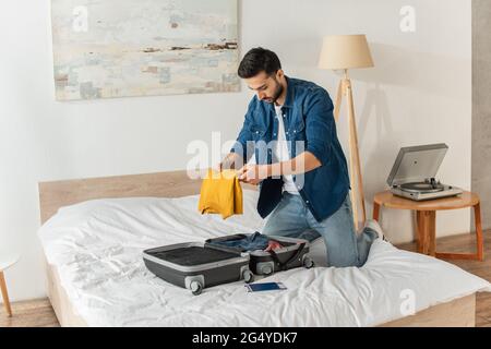 Junge Touristen, die ihre Kleidung in Koffer neben dem Flugticket und dem Pass auf das Bett legen Stockfoto