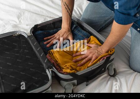 Kurzer Blick auf den Mann, der im Schlafzimmer Kleidung im Koffer drückt Stockfoto