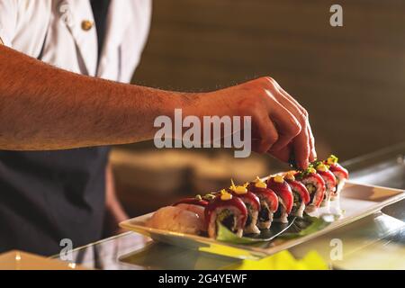 Professioneller Sushi-Koch, der Sushi-Brötchen dekoriert und in der Geschäftsküche auf dem Teller serviert wird. Stockfoto