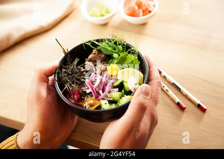 Ein Mann hält einen Poke-Salat mit Rindfleisch in einer Schüssel in den Händen. Zutaten Rindfleisch, Nameko-Pilze, Kirschtomaten, Reis, Gurke, Rote Zwiebel, Sesam Stockfoto