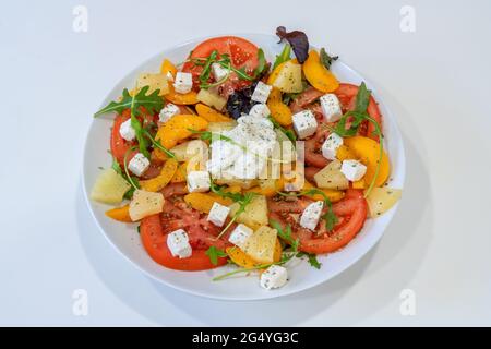 Vegetarischer Salat mit frischem Gemüse auf einem weißen Teller, Mozzarella-Käse. Weißer Hintergrund. Nahaufnahme. Draufsicht. Stockfoto