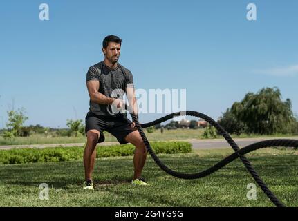 Männlicher Athlet im Freien im Park, Übungen für Ausdauer, mit einem dicken Seil, für Cross-Fitness. Europäisch Stockfoto