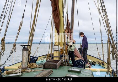 Lernen der Seile: Zwei Passagiere auf dem Segelkahn „Edith May“ helfen dem Skipper Ed Gransden bei einer Reise in die Themsemündung in Kent, England, ein Segel zu heben. Stockfoto