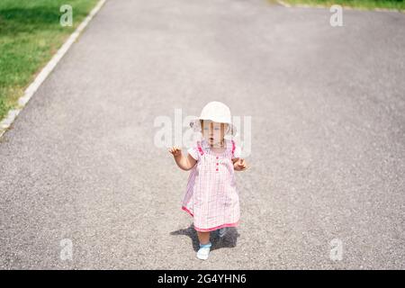 Kleines Mädchen in Kleid und Hut läuft auf dem Asphalt Stockfoto