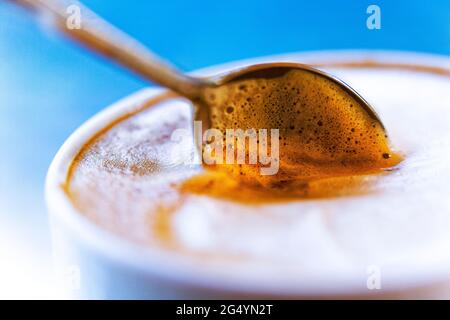 Cafe Latte (caffè e Latte) Espresso mit schaumiger Milch und Löffel in einer Tasse, fotografiert mit einer Lensbaby Composer Linse für einen weichen Fokus-Effekt Stockfoto