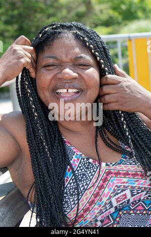 Posierte Porträt einer fröhlich lachenden attraktiven nigrischen Amerikanerin mit langen Haarverlängerung. In Brighton Beach, Brooklyn, New York City. Stockfoto