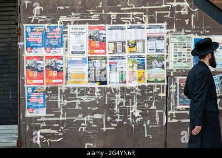 Ein chassidischer Jude passiert eine Wand von Anzeigen und Mitteilungen, die hauptsächlich auf Jiddisch sind. In der Rodney Street in Williamsburg, Brooklyn, New York. Stockfoto