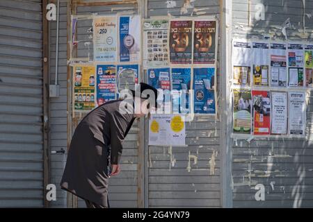 Ein junger orthodoxer Jude, wahrscheinlich ein Satmar, sieht sich Plakatwerbung an, die meist in Jiddisch ist. Auf der Lee Avenue in Williamsburg, Brooklyn, NYC. Stockfoto