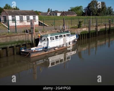 Altes verwittertes Boot liegt am längsten an der Kaimauer und reflektiert sich im Wasser Stockfoto