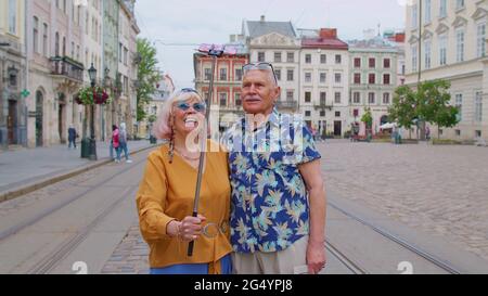 Ältere alte Touristen Mann mit Frau, die mit dem Smartphone auf einem Selfie-Stick in der Stadt unterwegs ist und Fotos fotografiert Stockfoto
