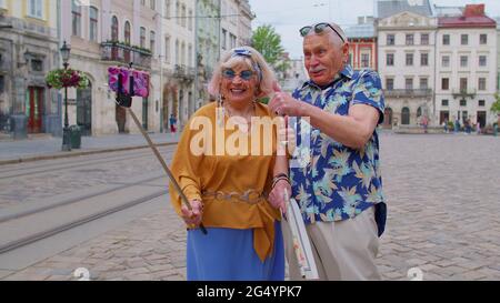 Ältere alte Touristen Mann mit Frau, die mit dem Smartphone auf einem Selfie-Stick in der Stadt unterwegs ist und Fotos fotografiert Stockfoto