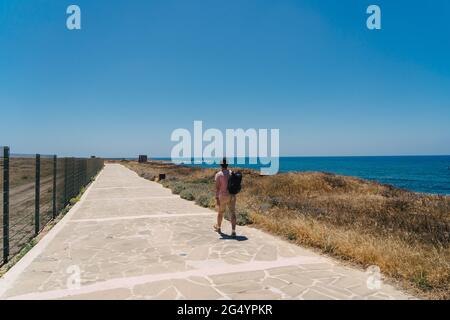 Mann Tourist mit Rucksack Spaziergang entlang Wanderweg an der felsigen Küste des Mittelmeers in der Stadt Paphos von Zypern im Sommer sonnig heißes Wetter. Küste Stockfoto