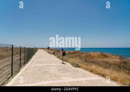 Mann Tourist mit Rucksack Spaziergang entlang Wanderweg an der felsigen Küste des Mittelmeers in der Stadt Paphos von Zypern im Sommer sonnig heißes Wetter. Küste Stockfoto