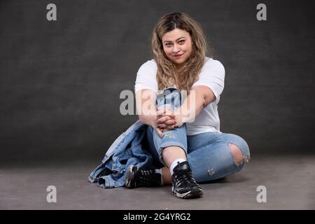 Schöne fette Frau in Denim-Kleidung auf grauem Hintergrund. Plus Größe Modell Mädchen. Stockfoto