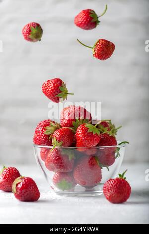 Schwebender frischer, reifer, köstlicher Erdbeeren in einer Glasschüssel auf grauem Hintergrund Stockfoto