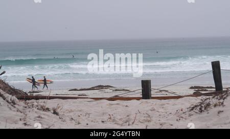 Monterey, Kalifornien USA - 13 Dec 2020: Surfer mit Surfbrettern, Sandstrand. Menschen surfen, neblige Küste im Dunst. Neblig regnerisch grau Herbst oder wi Stockfoto